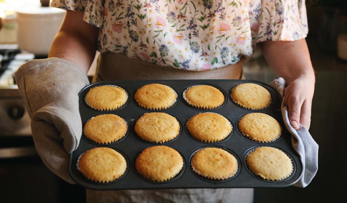 A woman holding pan full of freshly-baked muffins.