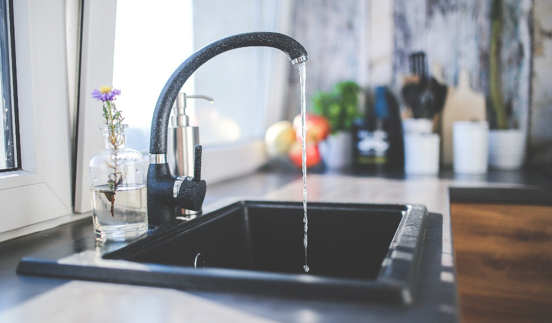 A black kitchen sink with water running from the curved black faucet.
