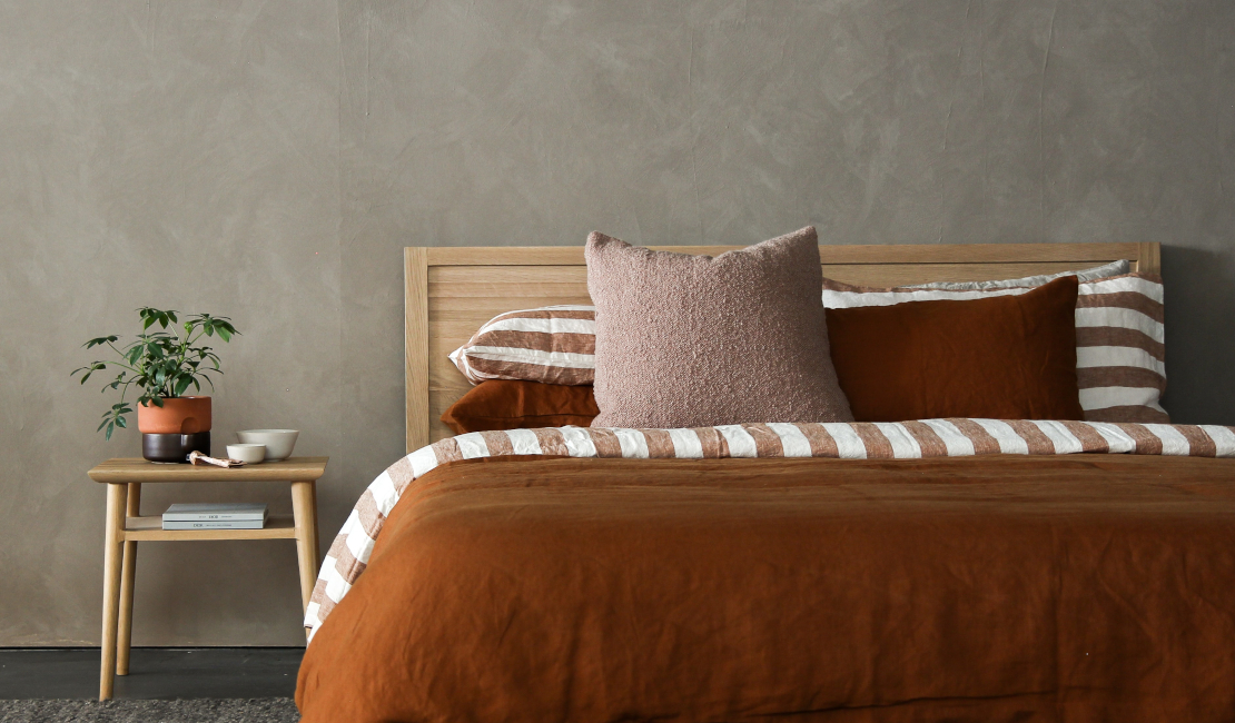 A beautiful rust coloured bed set with a potplant on the nightstand. 