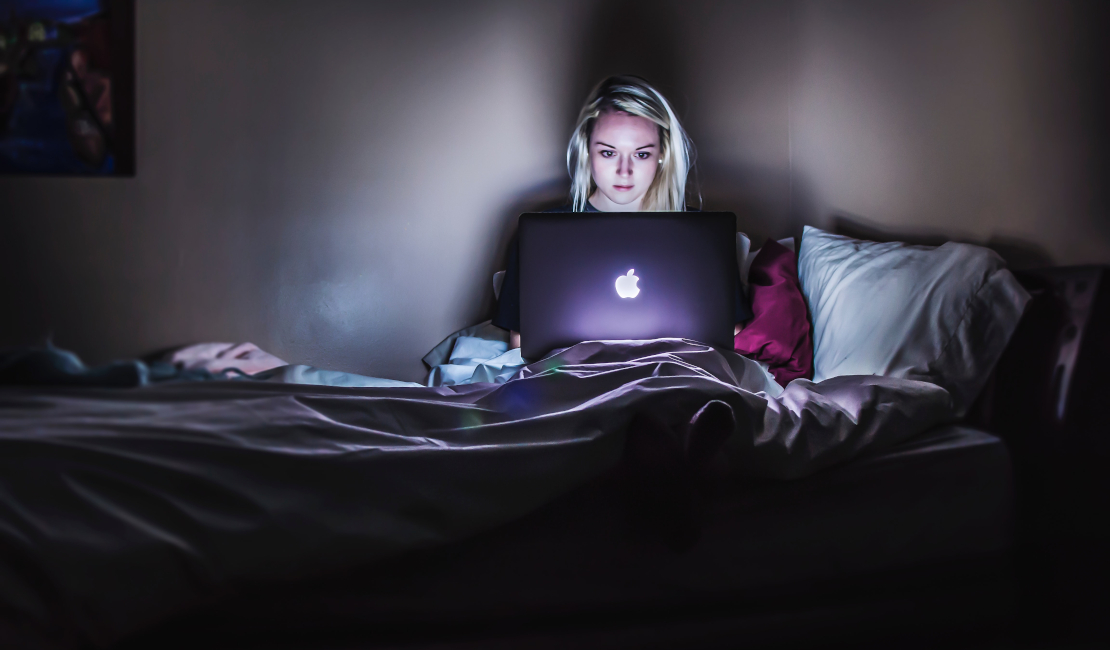 Woman sitting in bed, working on an Apple laptop.