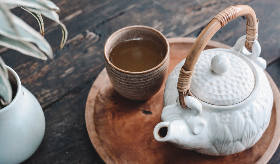 A cup of tea next to a porcelain teapot on a wooden tray.