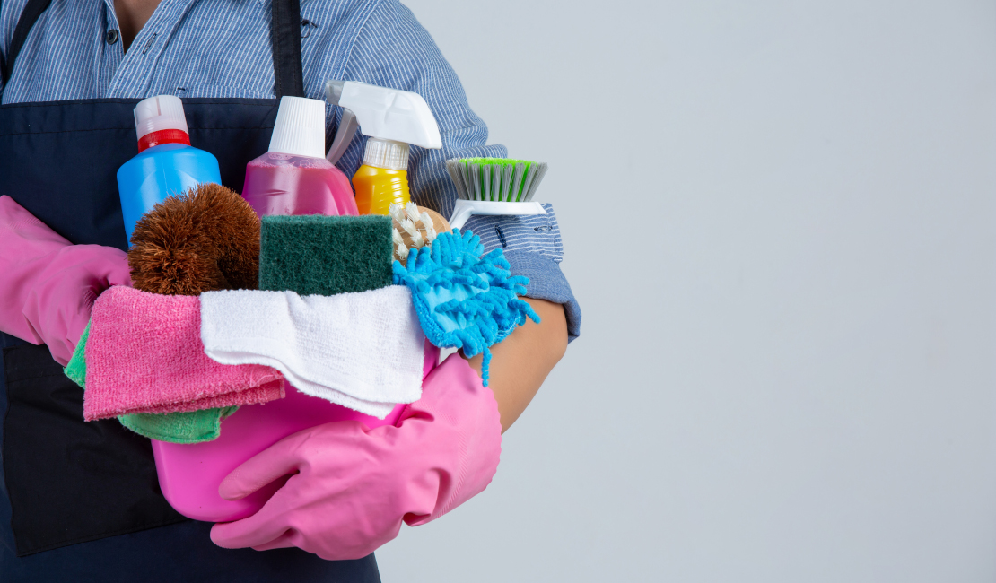 Person holding a bucket full of cleaning agents such as soap, cloths, and spunges.