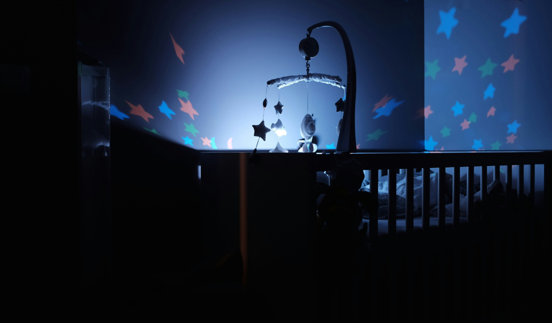 Baby bed in dark room with light shining on mobile.